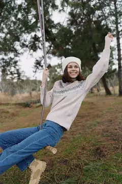 Улыбающаяся девушка в белой шапке качается на качелях в осеннем лесу