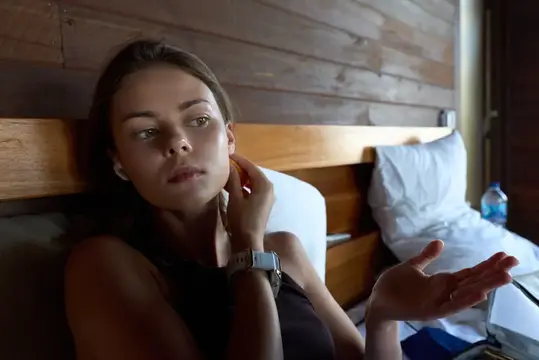 Молодая женщина в наушниках лежит на кровати и жестикулирует