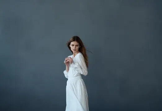 Молодая женщина в белом платье на сером фоне