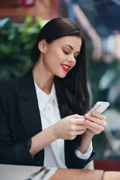 Улыбающаяся брюнетка в деловом костюме смотрит в смартфон
