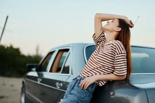 Молодая женщина с сигаретой отдыхает, опершись на старый автомобиль