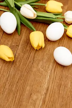 Белые яйца и жёлтые тюльпаны на деревянном столе