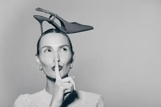 Молодая женщина с туфлей на голове прикладывает палец к губам