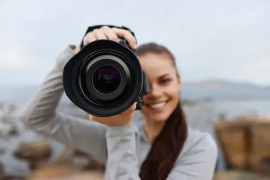 Жизнерадостная молодая женщина с фотоаппаратом на природе у моря, воплощающая любовь к фотографии и приключениям