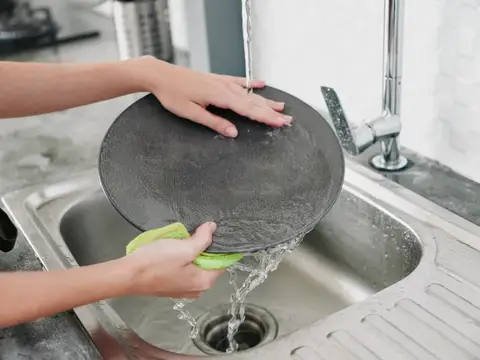 Женщина моет чугунную сковороду под краном на кухне