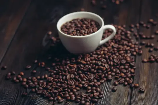Чашка с блюдцем и кофейные зерна на деревянном фоне, передающие аромат