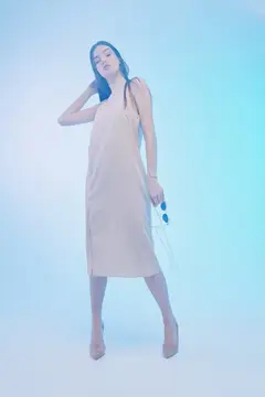Молодая женщина в бежевом платье позирует на голубом фоне