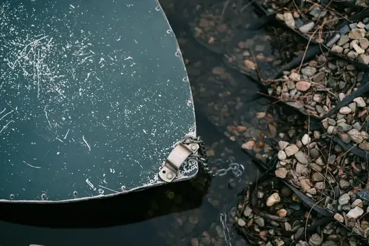 Металлическая крышка с цепью у каменистого берега водоёма