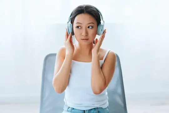 Молодая азиатская девушка в наушниках слушает музыку дома