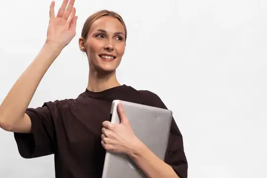 Улыбающаяся светловолосая девушка с ноутбуком машет рукой на белом фоне