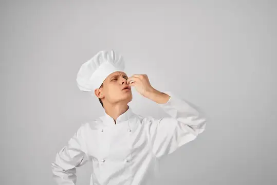 Молодой повар в белом колпаке пробует соус на вкус