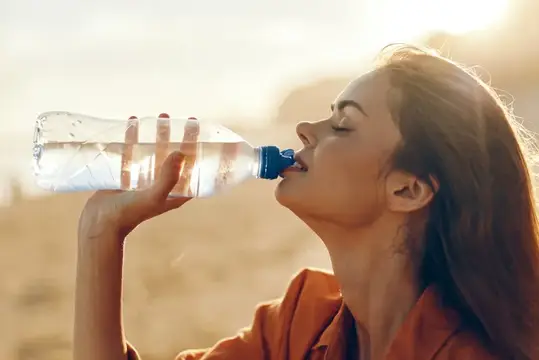 Молодая женщина пьёт воду на открытом воздухе в ярком солнечном свете