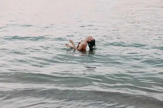 Девушка с темными волосами плавает на спине в спокойной воде