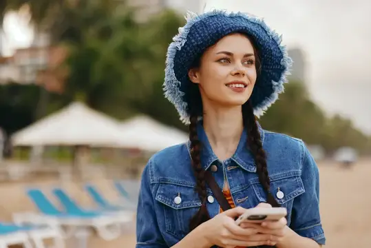 Улыбающаяся девушка в джинсовой куртке и вязаной панаме на пляже