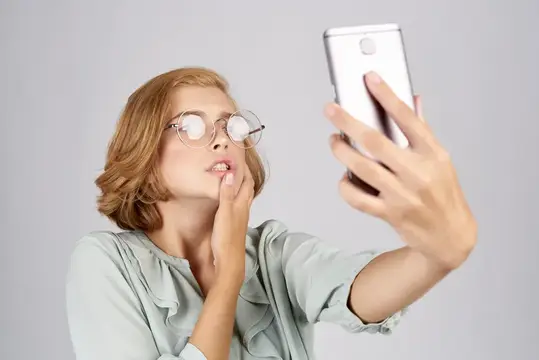 Женщины с мобильным телефоном в руках фотографируют себя в рубашке на светлом фоне