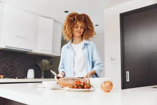 Кудрявая женщина режет помидоры на светлой кухне