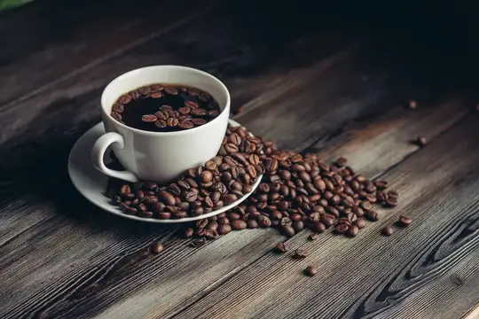 Блюдце с кофейными зернами и белая чашка на деревянном столе