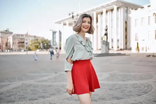 Милая блондинка в красной юбке на улице, позирует на прогулке