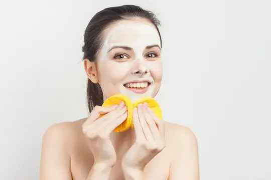 Улыбающаяся девушка с белой маской на лице держит две жёлтые губки