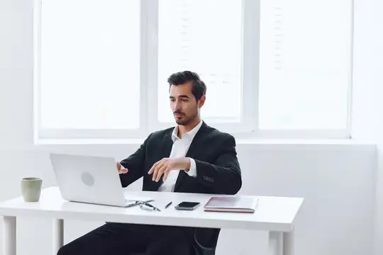 Молодой мужчина в деловом костюме работает за ноутбуком в светлом офисе