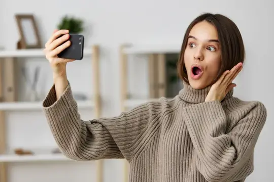 Удивленная девушка делает селфи на смартфон дома