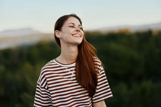 Улыбающаяся девушка с длинными волосами на фоне зелёных холмов