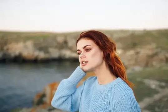 Рыжеволосая девушка в голубом свитере на фоне моря
