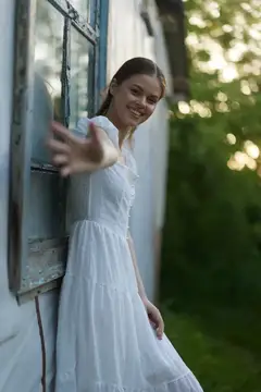 Улыбающаяся девушка в белом платье у окна старого дома