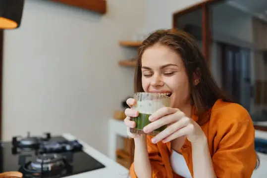 Молодая женщина с наслаждением пьёт зелёный смузи на кухне