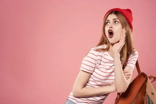 Удивлённая девушка в красной шапке на розовом фоне