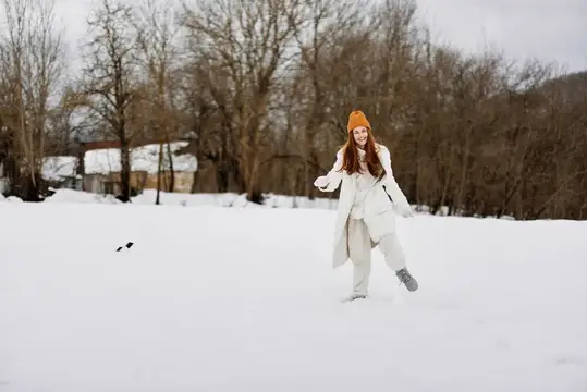 Рыжеволосая девушка в оранжевой шапке гуляет по зимнему полю