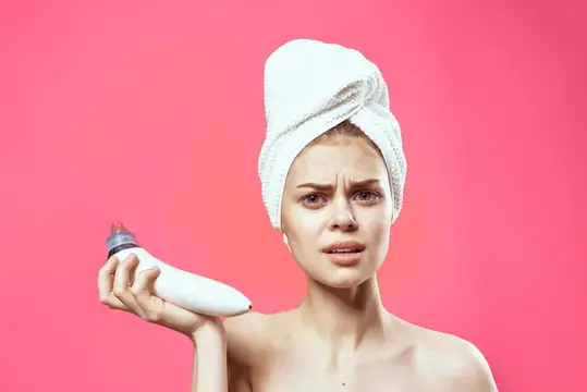 Веселая женщина с полотенцем на голове делает вакуумную чистку лица на розовом фоне