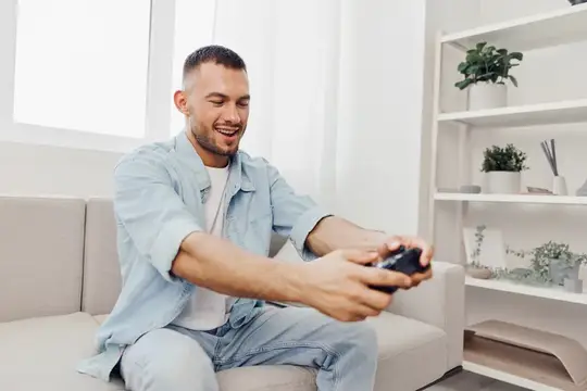 Улыбающийся мужчина играет в видеоигру на диване