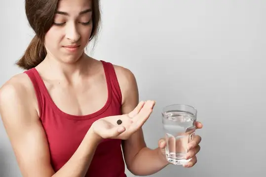 Молодая женщина держит капсулу и стакан воды