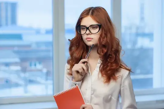 Рыжеволосая девушка в очках с блокнотом у окна офиса