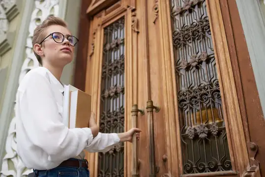 Девушка в очках с книгой открывает старинную деревянную дверь