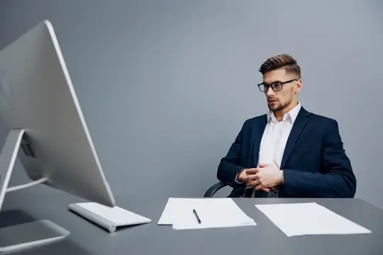 Молодой мужчина в очках и деловом костюме работает за компьютером