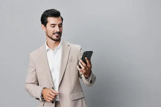 Уверенный молодой бизнесмен в костюме улыбается, держа смартфон и глядя на него