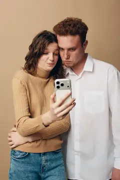 Пара смотрит в смартфон с серьёзным видом на бежевом фоне