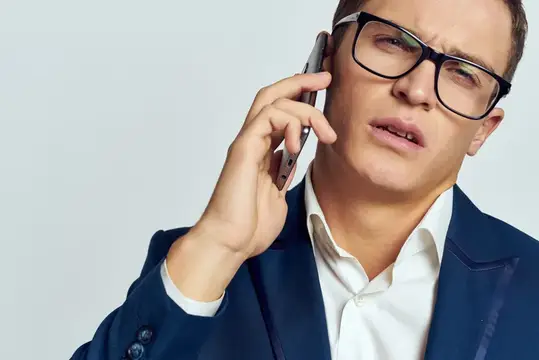 Деловой мужчина в костюме и очках разговаривает по телефону, рядом с ним документы, технологии, официальный стиль