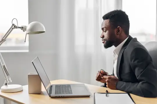 Темнокожий мужчина в костюме работает за ноутбуком в офисе