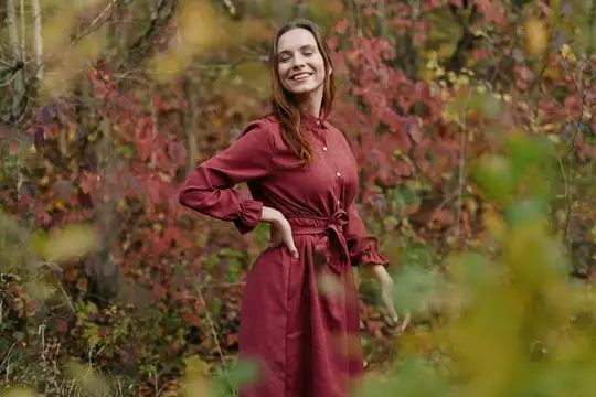 Улыбающаяся женщина в бордовом платье среди осенних кустов
