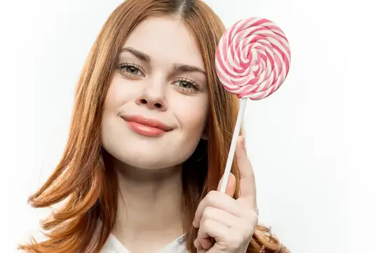 Рыжеволосая девушка с большой розовой леденцовой конфетой на белом фоне