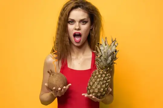 Удивлённая девушка с кокосом и ананасом на жёлтом фоне