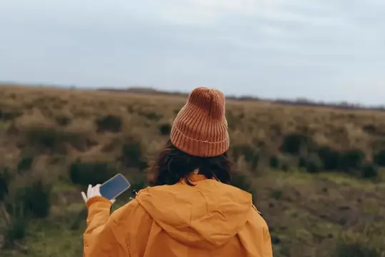 Девушка в рыжей шапке фотографирует пейзаж на телефон