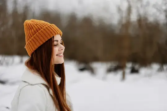 Улыбающаяся девушка в оранжевой шапке на зимней прогулке