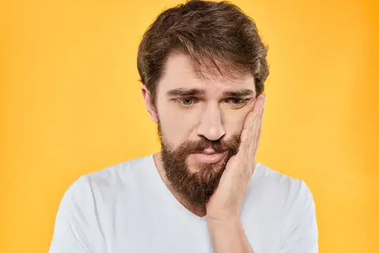 Задумчивый бородатый мужчина в белой футболке на жёлтом фоне