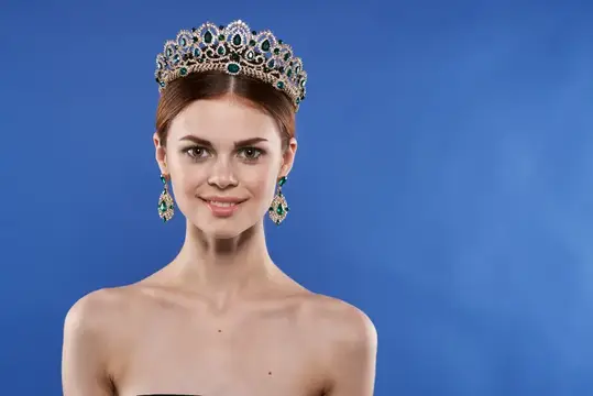 Модель в образе принцессы с короной на голове, макияжем и жестом руки на синем фоне