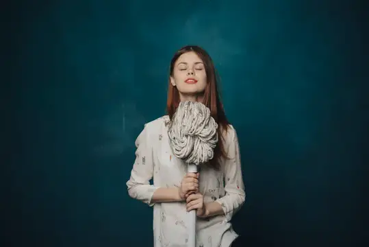 Молодая женщина с закрытыми глазами обнимает швабру на тёмно-зелёном фоне