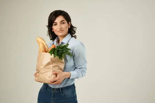 Молодая женщина с бумажным пакетом продуктов на светлом фоне